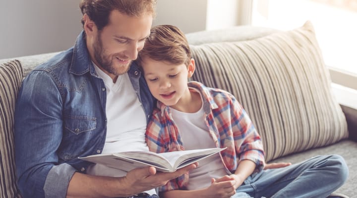 Father and son reading a book together on a sofa