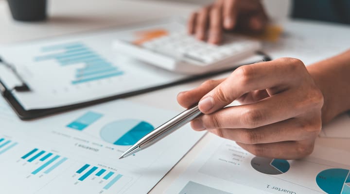 Table filled with paper with graphs and pie charts on as someone uses a calculator