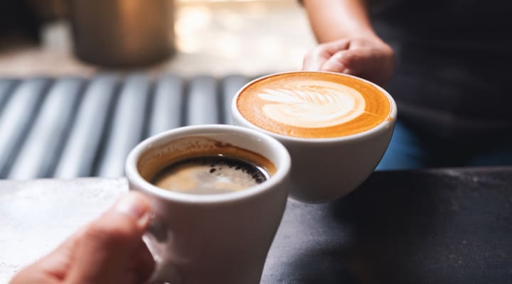 Close up of two people holding coffee cups in a cafe