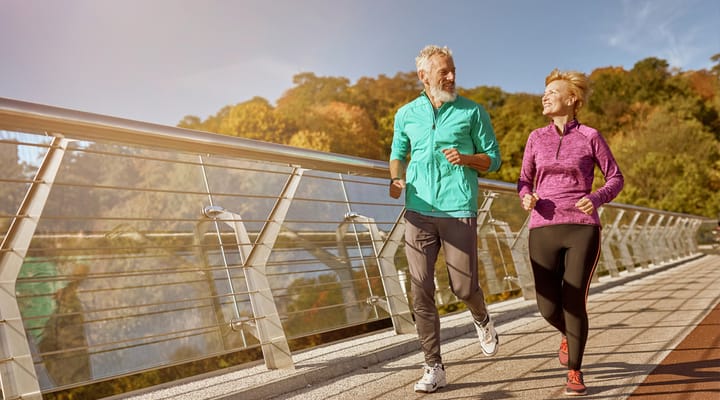 A mature couple jogging across a bridge.