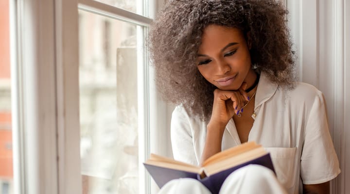 A young woman sitting in a window reading a book.