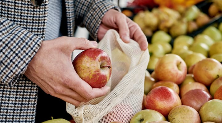 A shopper using a reusable muslin bag to purchase apples.