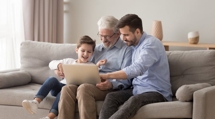 A grandfather using a laptop with his adult son and grandchild.