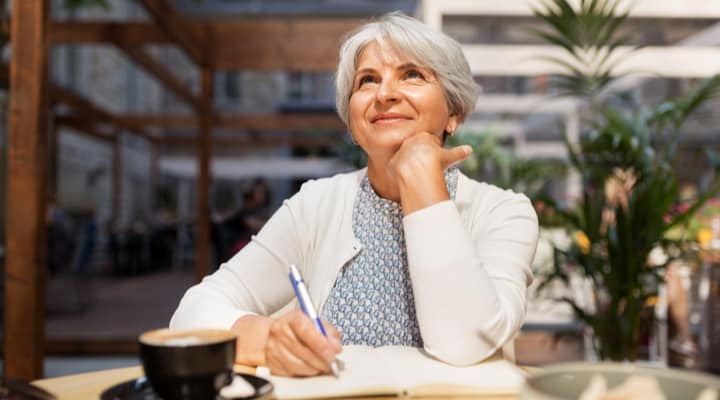 An older woman enjoying a cup of coffee and writing in a journal.