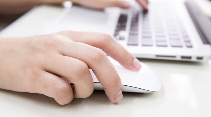 A person typing on a laptop keyboard and using a mouse.