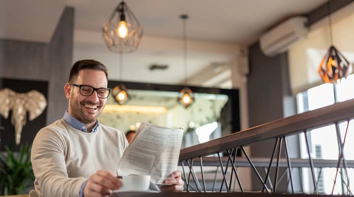 A man reading a newspaper while drinking coffee.