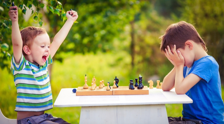 two boys playing chess, one has just won the game and is celebrating