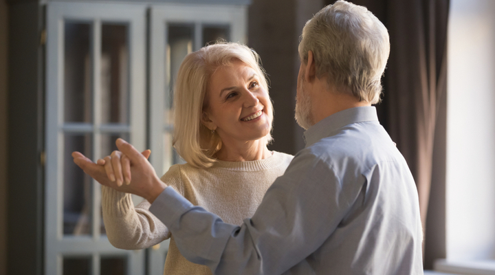 A smiling senior couple dance in their living room