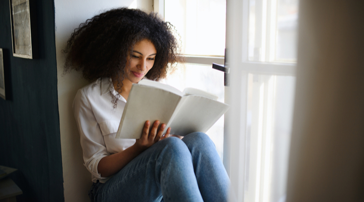 A woman sitting in a window and reading a book.