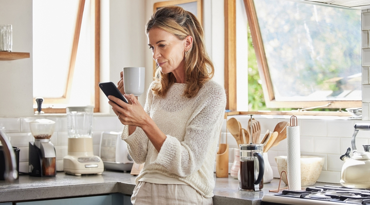 A woman drinking a coffee while looking at her phone.