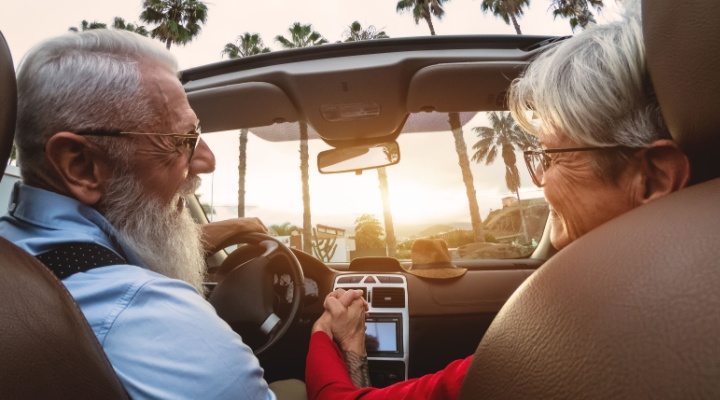 A happy older couple driving in a convertible car.