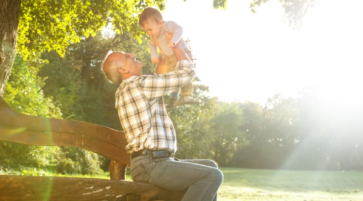 A grandfather playing with his young grandson in a park.